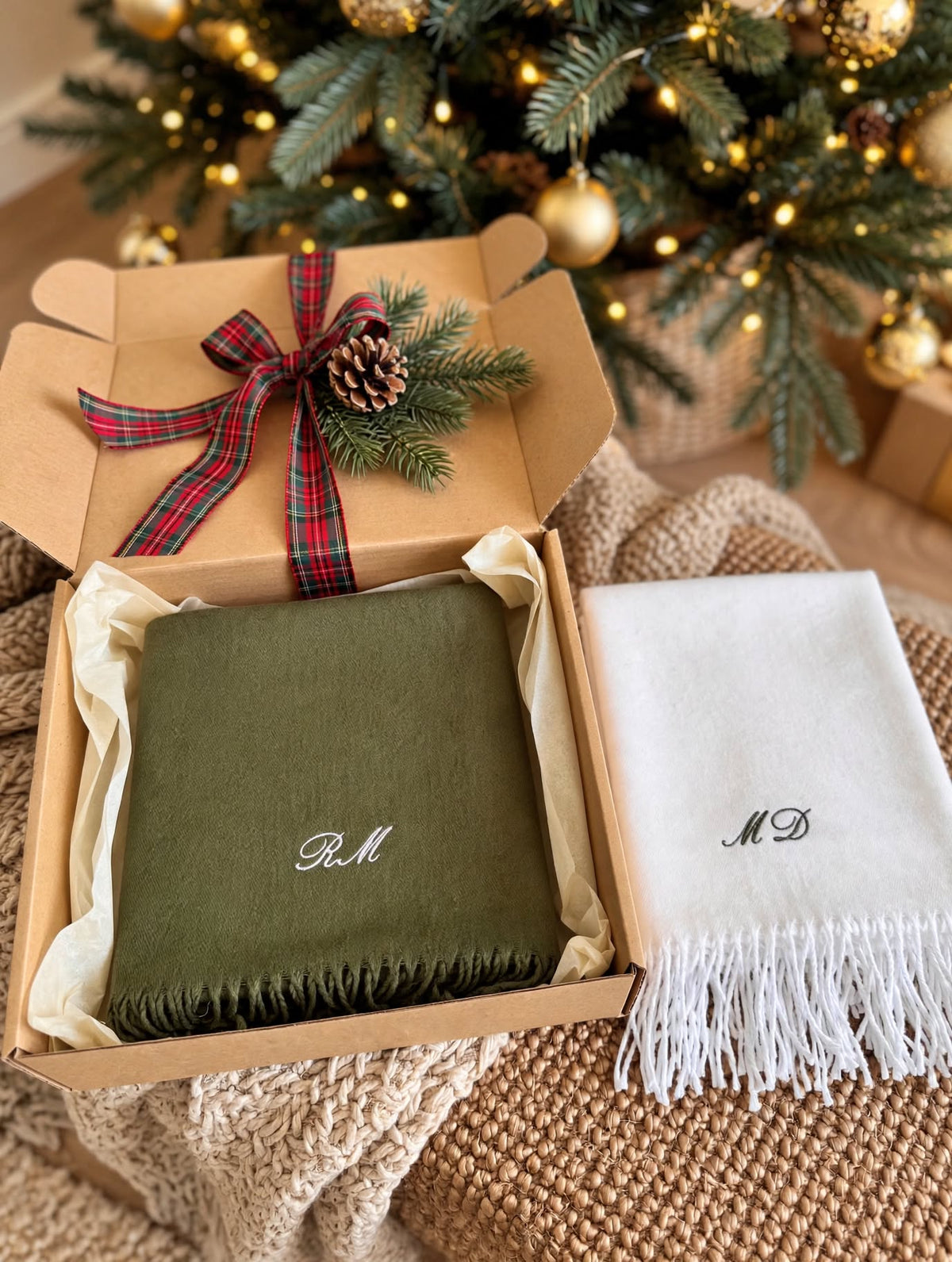 Écharpes vert sapin et blanche brodées d’initiales dans une boîte cadeau au pied du sapin