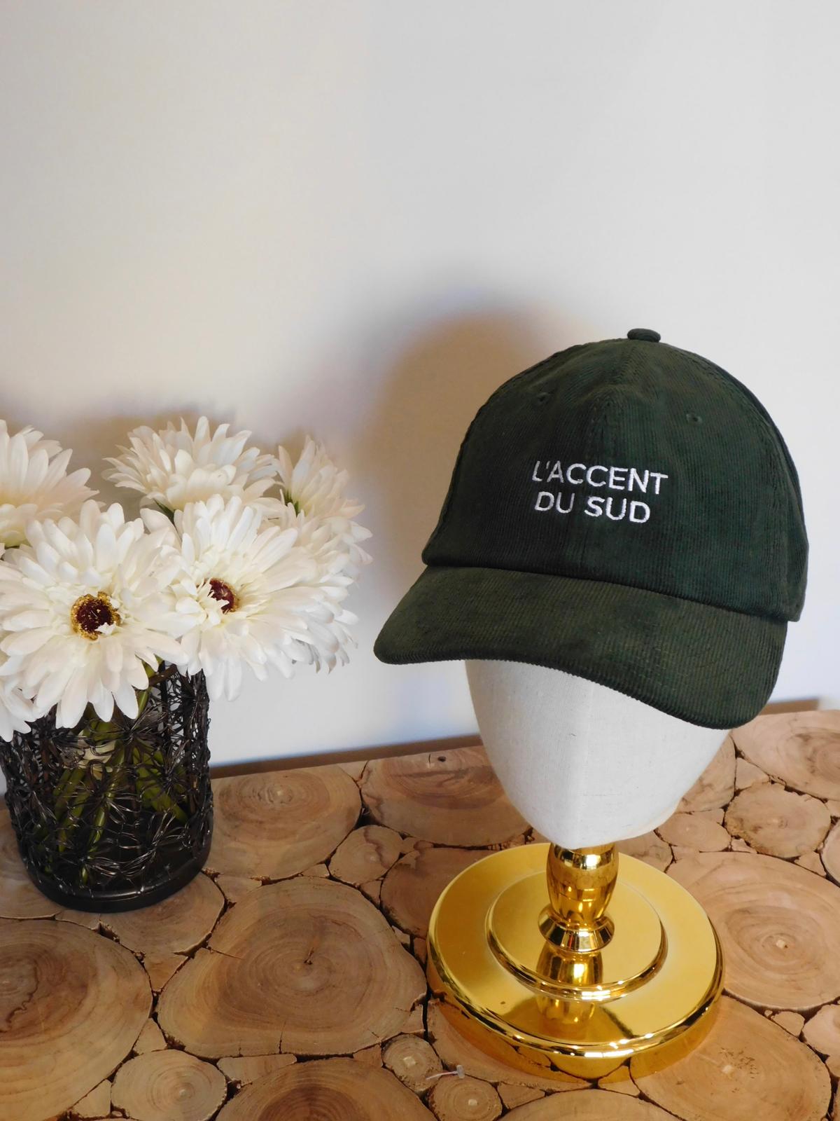 Casquette en velours côtelé vert sapin brodée L'accent du sud en fil blanc, sur une tête de présentation dorée