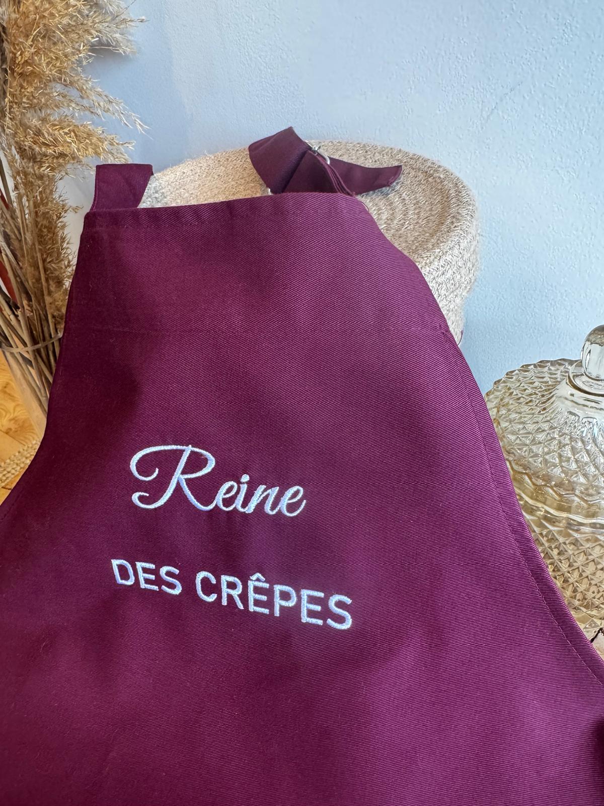 Tablier bordeaux brodé Reine des crêpes posé sur un panier en jute